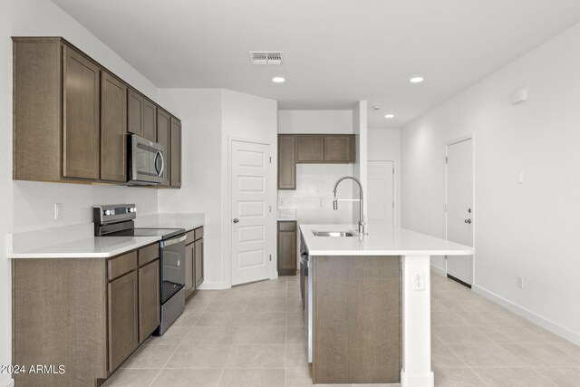 kitchen featuring light tile patterned flooring, a center island with sink, black electric range oven, and sink