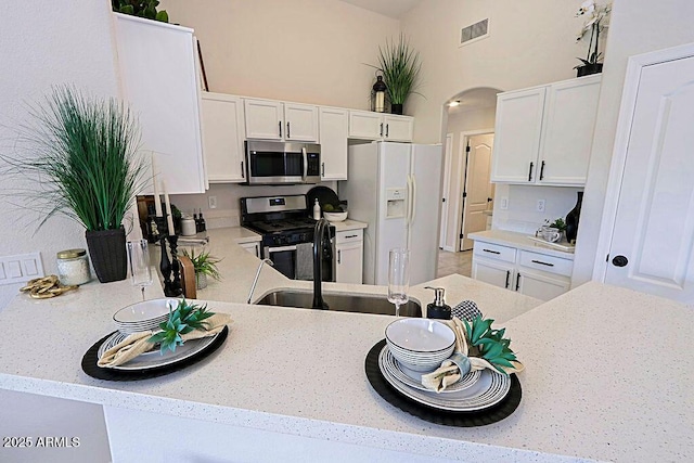 kitchen featuring sink, white cabinetry, stainless steel appliances, light stone counters, and kitchen peninsula