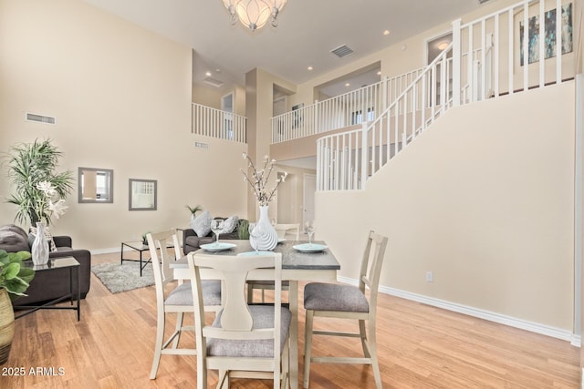 dining area featuring visible vents, a towering ceiling, wood finished floors, baseboards, and stairway