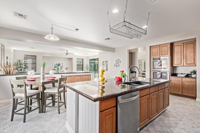 kitchen with brown cabinetry, visible vents, appliances with stainless steel finishes, a center island with sink, and a sink