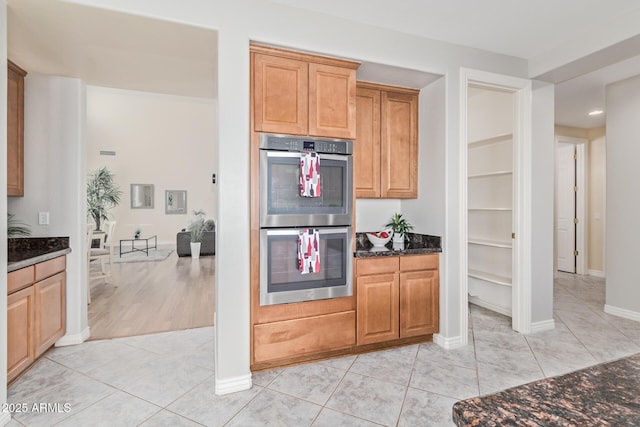 kitchen with light tile patterned flooring, stainless steel double oven, dark stone countertops, recessed lighting, and baseboards