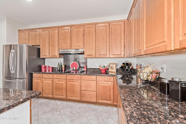 kitchen with freestanding refrigerator, light tile patterned floors, under cabinet range hood, dark stone countertops, and backsplash