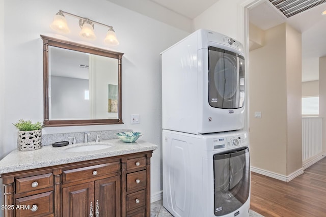 laundry area with laundry area, stacked washer and clothes dryer, baseboards, light wood-style floors, and a sink