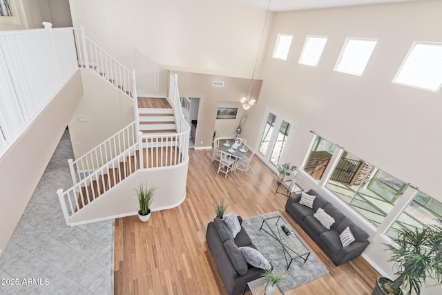 living area with visible vents, wood finished floors, stairway, baseboards, and a high ceiling