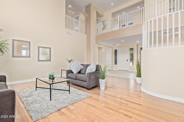living area featuring a towering ceiling, visible vents, wood finished floors, baseboards, and recessed lighting