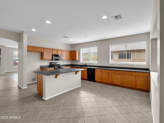 kitchen featuring gas range, light tile patterned floors, black dishwasher, a breakfast bar area, and a kitchen island