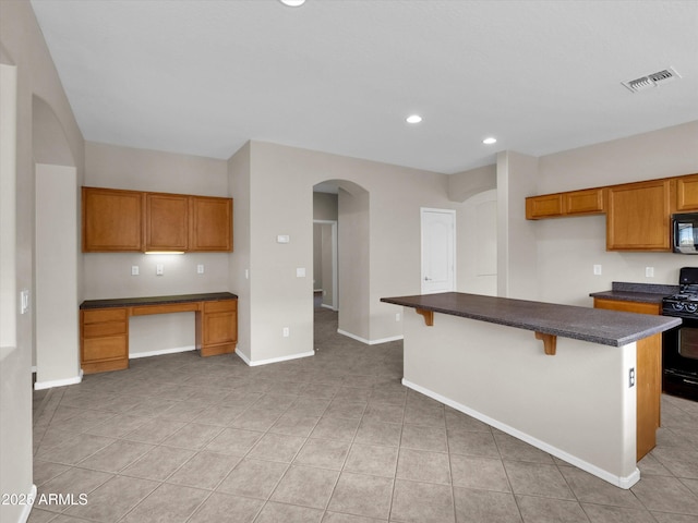 kitchen featuring a center island, built in desk, a breakfast bar area, light tile patterned flooring, and black appliances