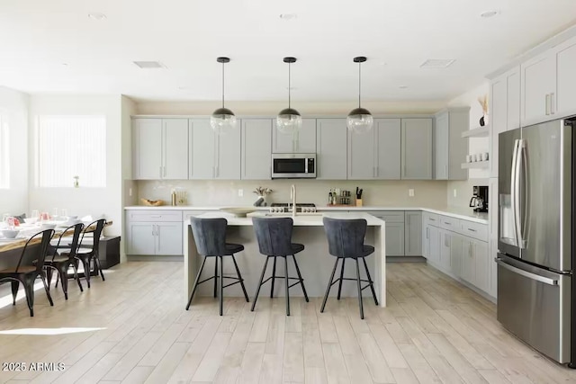 kitchen featuring a kitchen bar, a center island with sink, stainless steel appliances, gray cabinetry, and hanging light fixtures