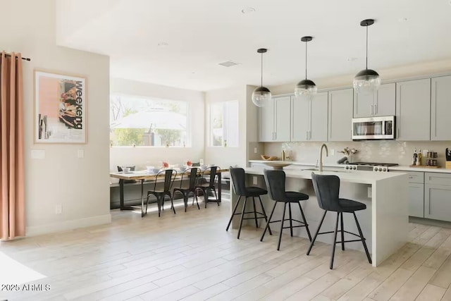 kitchen featuring light wood-type flooring, gray cabinets, decorative light fixtures, and a kitchen island with sink