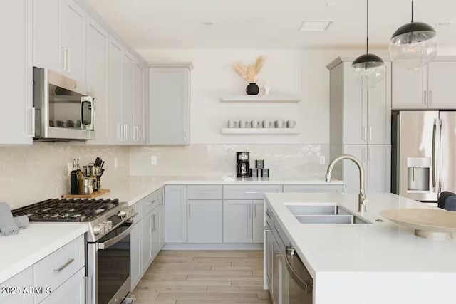 kitchen with light hardwood / wood-style floors, pendant lighting, decorative backsplash, sink, and stainless steel appliances