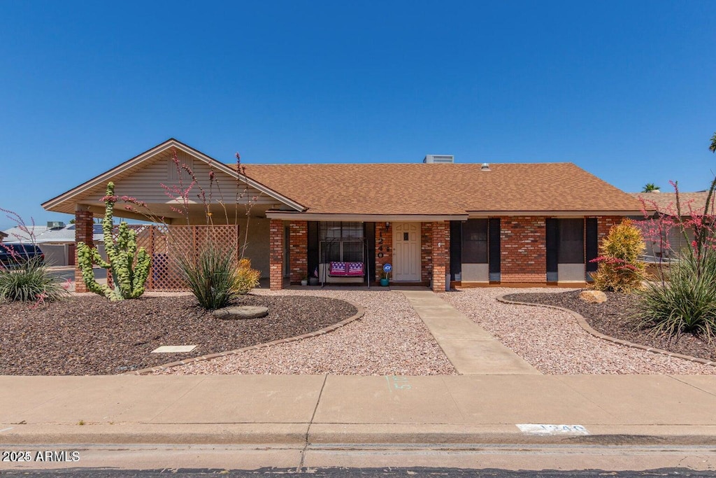 ranch-style house featuring covered porch, a shingled roof, and brick siding
