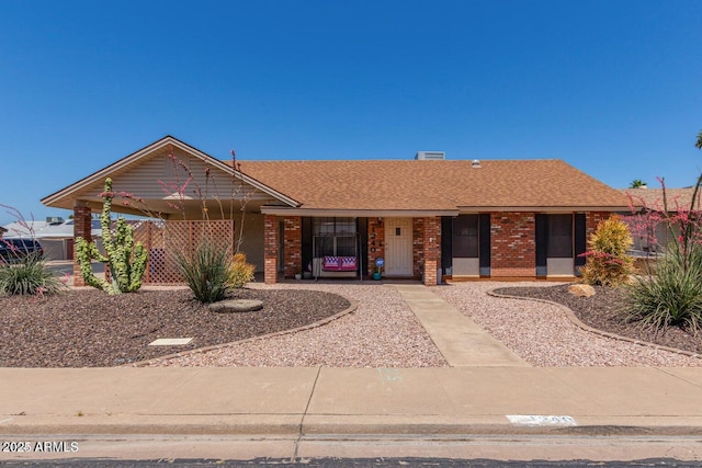 ranch-style house featuring covered porch, a shingled roof, and brick siding