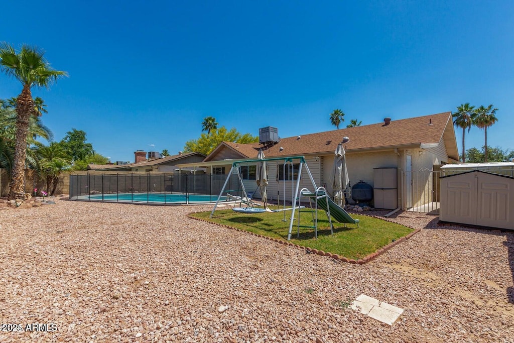 rear view of house with an outdoor structure, a fenced backyard, a fenced in pool, a playground, and a storage shed