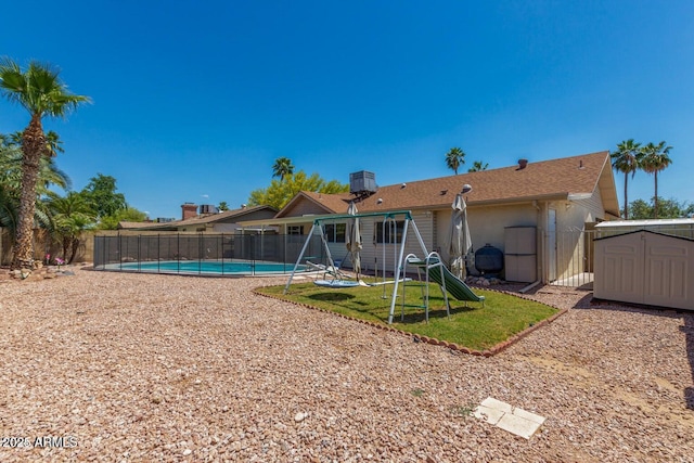 rear view of house with an outdoor structure, a fenced backyard, a fenced in pool, a playground, and a storage shed