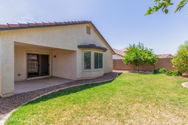 rear view of house with a tile roof, a fenced backyard, a lawn, a patio, and stucco siding
