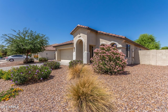 mediterranean / spanish house with a tiled roof, concrete driveway, fence, a garage, and stucco siding
