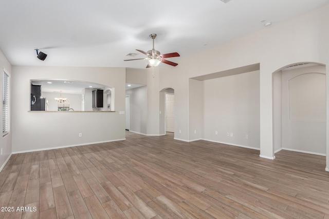 unfurnished living room with arched walkways, wood finished floors, baseboards, and ceiling fan