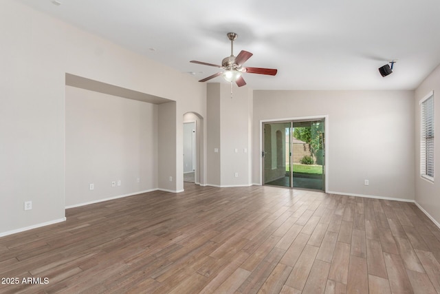 spare room featuring arched walkways, vaulted ceiling, baseboards, a ceiling fan, and wood finished floors