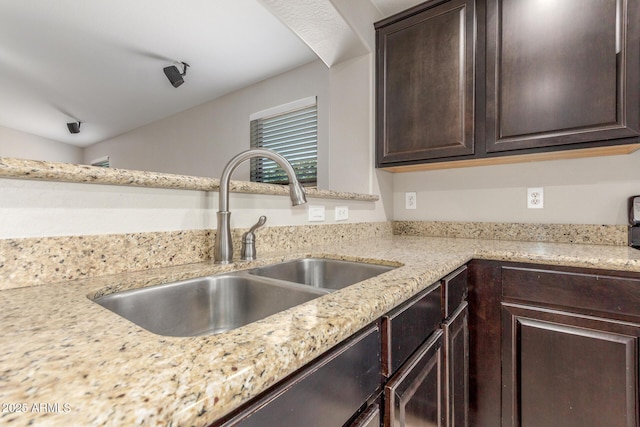 kitchen with dark brown cabinetry, light stone countertops, and a sink