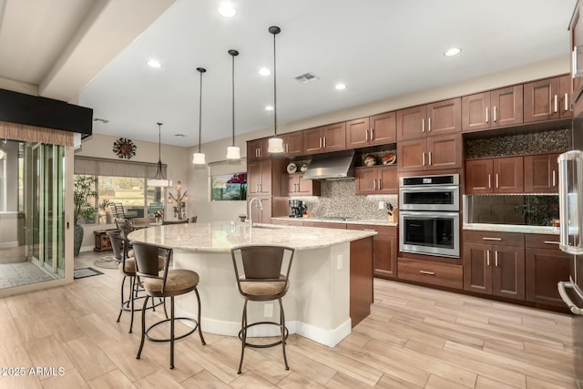 kitchen with tasteful backsplash, stainless steel double oven, a sink, and under cabinet range hood