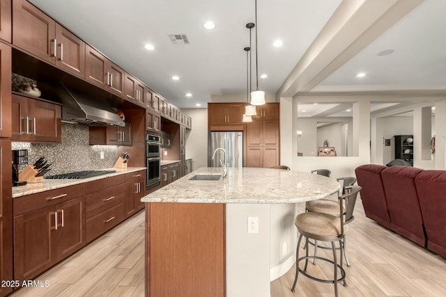 kitchen featuring light wood finished floors, appliances with stainless steel finishes, a breakfast bar area, a sink, and backsplash