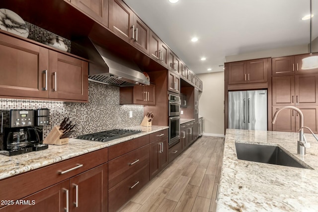 kitchen featuring tasteful backsplash, light wood-style flooring, appliances with stainless steel finishes, light stone countertops, and a sink