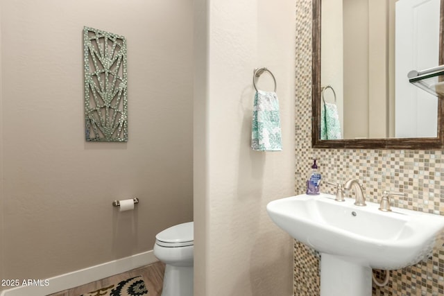 half bathroom with toilet, a sink, wood finished floors, baseboards, and tasteful backsplash