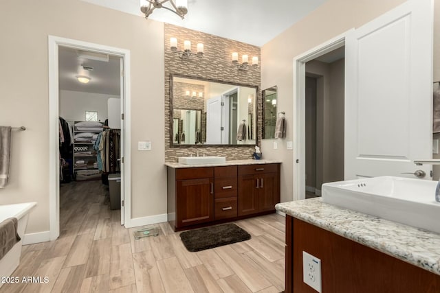 full bathroom featuring wood finished floors, tasteful backsplash, a sink, and a notable chandelier