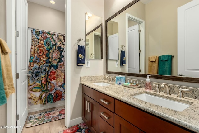 bathroom featuring double vanity, a shower with shower curtain, a sink, and baseboards