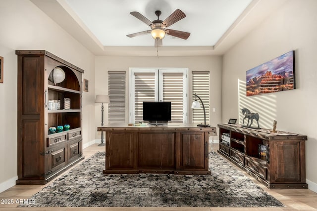 office space with a raised ceiling, ceiling fan, light wood finished floors, and baseboards