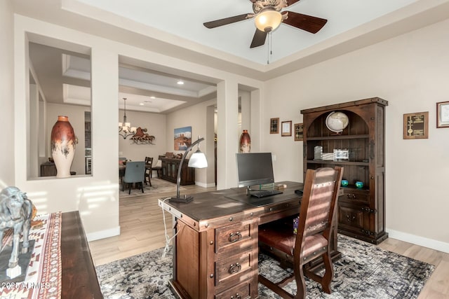 home office featuring light wood-style floors, a tray ceiling, baseboards, and ceiling fan with notable chandelier