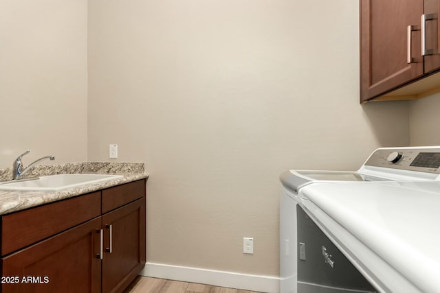 laundry area with cabinet space, baseboards, light wood-style flooring, separate washer and dryer, and a sink