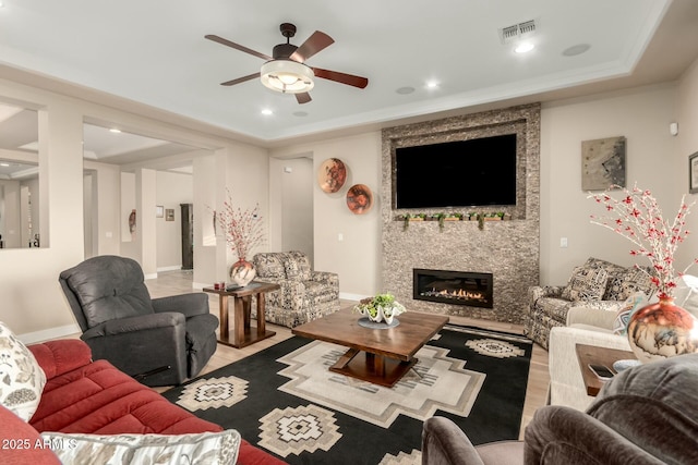 living area featuring a tray ceiling, recessed lighting, visible vents, a large fireplace, and ceiling fan