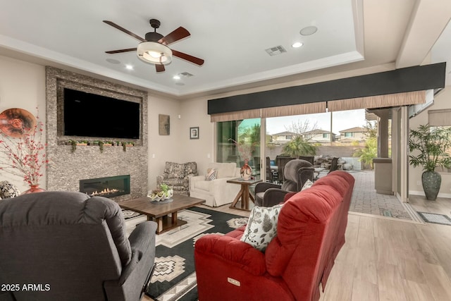 living area featuring a fireplace, a raised ceiling, visible vents, a ceiling fan, and wood finished floors