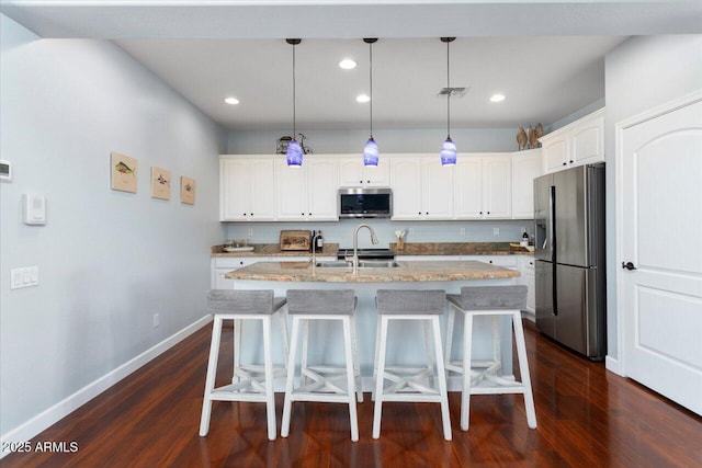 kitchen with decorative light fixtures, white cabinets, stainless steel appliances, and a kitchen island with sink