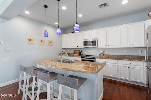 kitchen featuring pendant lighting, white cabinets, stainless steel appliances, an island with sink, and sink