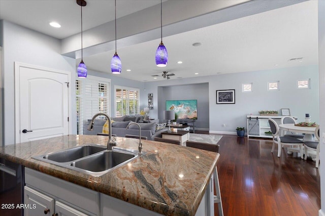 kitchen featuring a kitchen island with sink, dark hardwood / wood-style flooring, dark stone countertops, pendant lighting, and sink