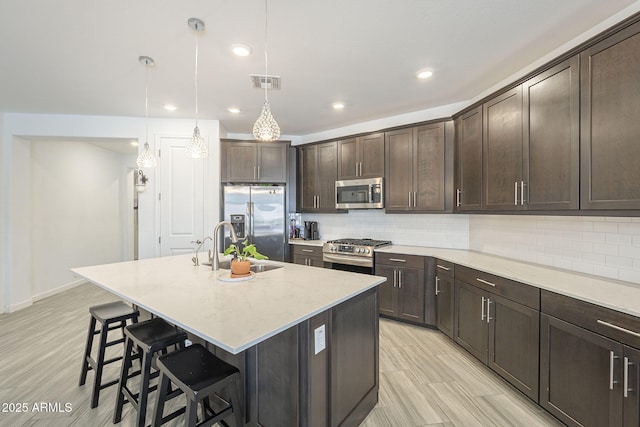 kitchen featuring stainless steel appliances, visible vents, decorative backsplash, dark brown cabinets, and a kitchen bar