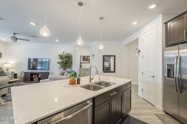 kitchen with light stone counters, dark brown cabinetry, stainless steel appliances, a sink, and open floor plan