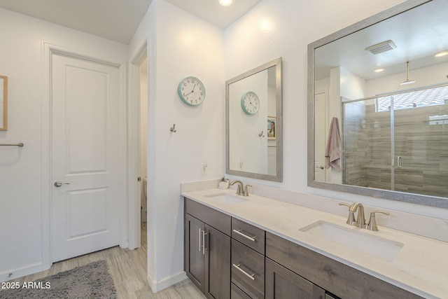 bathroom featuring visible vents, a sink, a shower stall, and double vanity