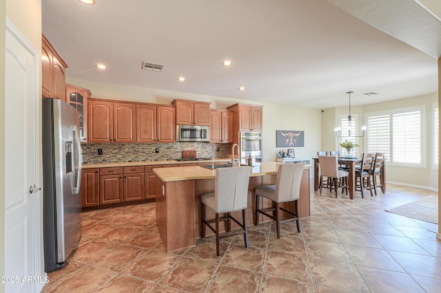 2514 E Grand Canyon Dr, Chandler, AZ 85249 - kitchen with appliances with stainless steel finishes, light countertops, decorative backsplash, a kitchen island with sink, and a breakfast bar
