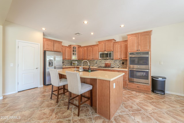 2514 E Grand Canyon Dr, Chandler, AZ 85249 - kitchen featuring appliances with stainless steel finishes, backsplash, a kitchen island with sink, glass insert cabinets, and recessed lighting
