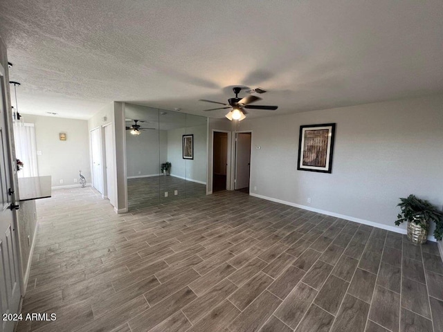 unfurnished living room featuring a textured ceiling, ceiling fan, and dark wood-type flooring