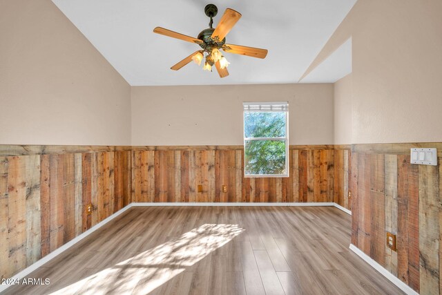 unfurnished room featuring wood walls, ceiling fan, and light hardwood / wood-style flooring