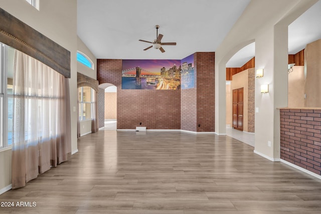 interior space with a towering ceiling, light hardwood / wood-style floors, brick wall, and ceiling fan