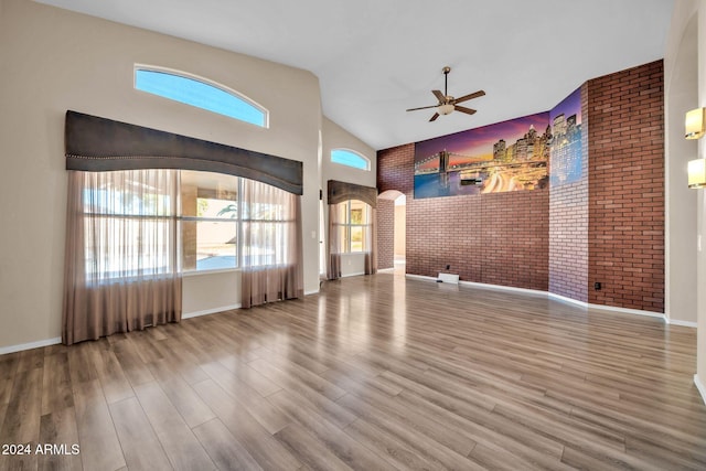 unfurnished living room featuring wood-type flooring, a healthy amount of sunlight, brick wall, and high vaulted ceiling