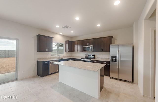 kitchen with light stone counters, a center island, a sink, dark brown cabinetry, and appliances with stainless steel finishes