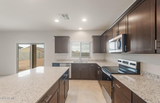 kitchen with a sink, dark brown cabinets, visible vents, light stone counters, and appliances with stainless steel finishes