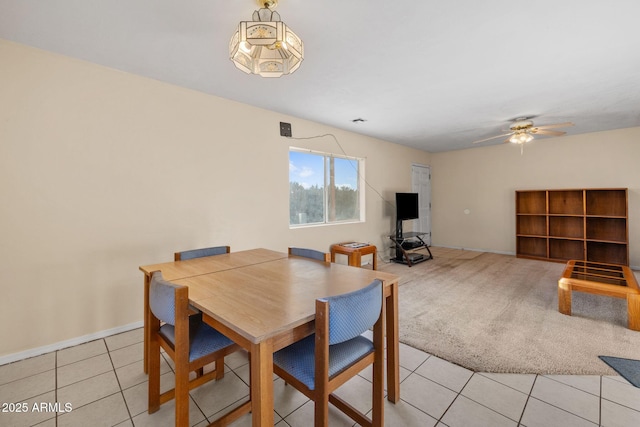 dining space with a ceiling fan, light carpet, baseboards, and light tile patterned floors