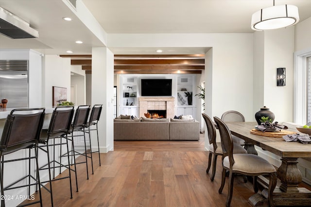 dining area featuring beamed ceiling, built in shelves, hardwood / wood-style flooring, and a tile fireplace